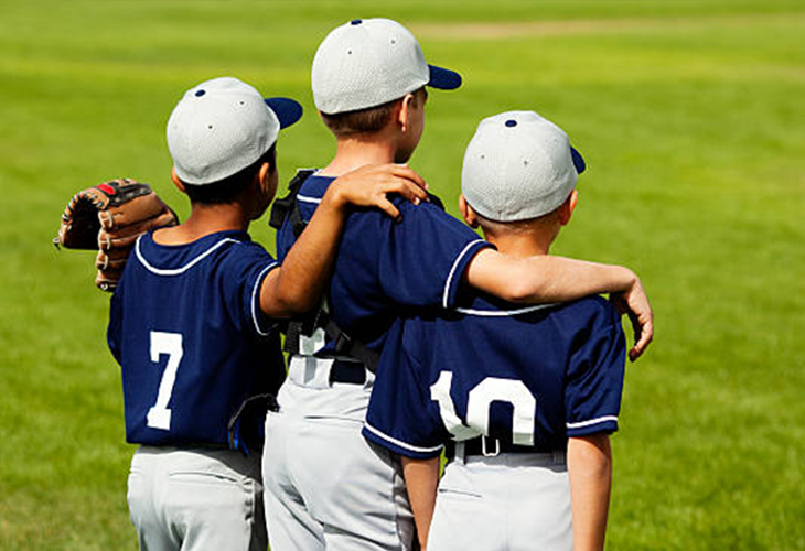 3 Youth Baseball Players standing in the outfield with their arms around each others shoulders