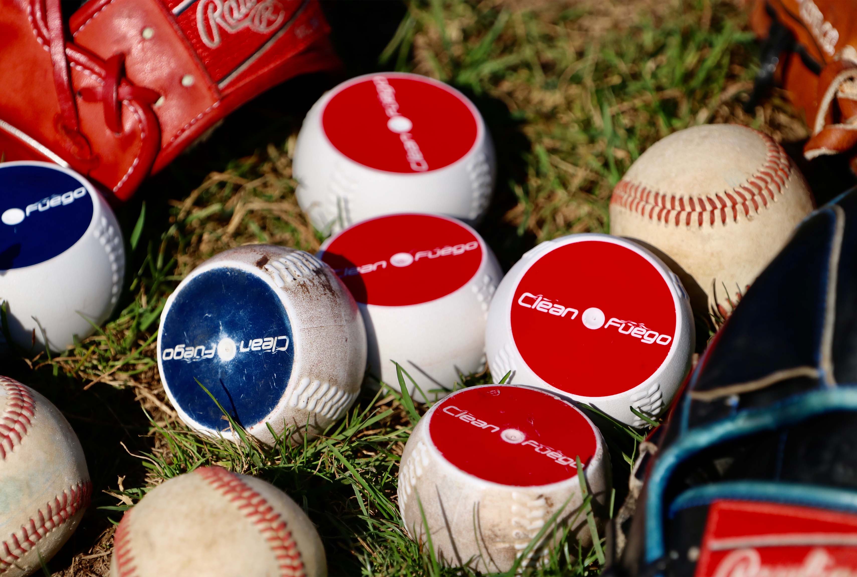 Group of CleanFuego baseballs sitting in grass next to a few baseball gloves