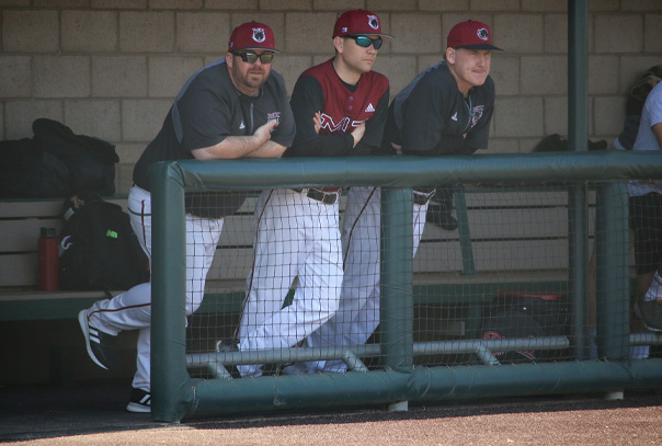 MIT coach Todd Carroll leaning on dugout railing alongside two others