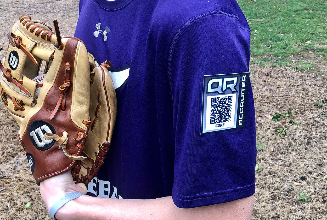 Youth baseball player in purple jersey turned to side with QR code on his glove-side sleeve