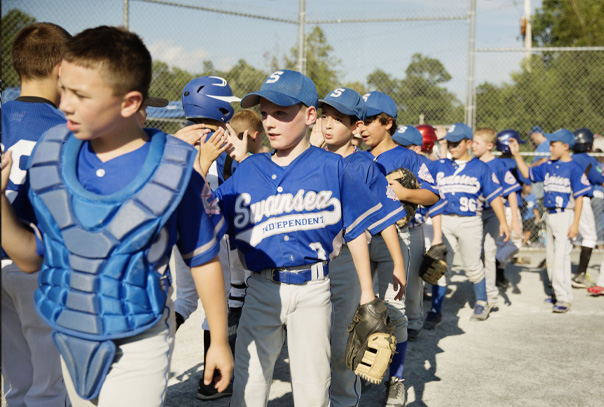 Two youth baseball teams wearing white & blue jerseys with the letter S on their cap high-fiving after a game