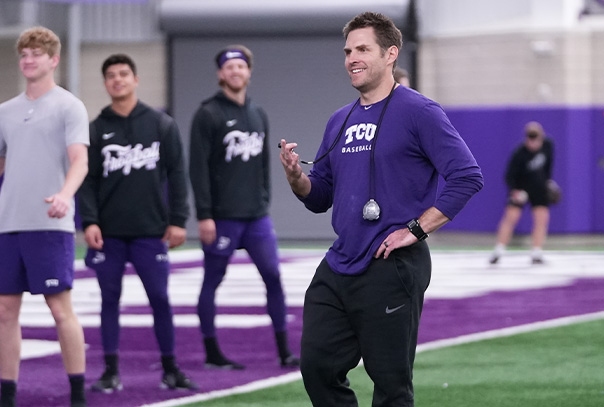 TCU strength coach Zach Dechant smiling while holding stopwatch with players in distant background