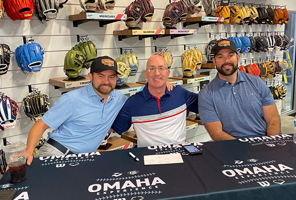 Kendall Rogers seated at table on far right next to D1Baseball's Aaron Fitt and Mike Rooney with wall of baseball gloves in background
