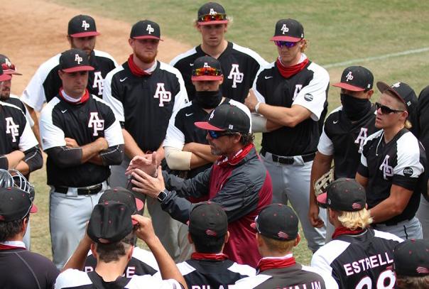 A baseball coach in middle of team huddled around him as he's speaking