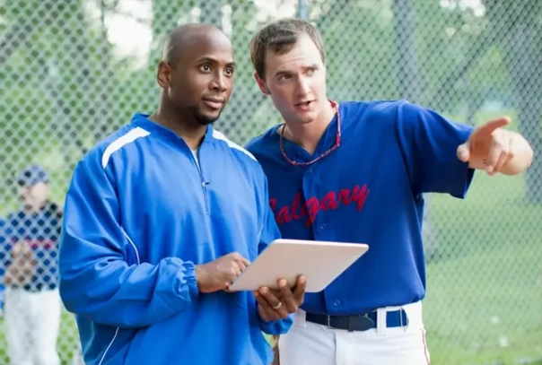 Two coaches talking to to each other. One is pointing out to the field and the other is looking that way.