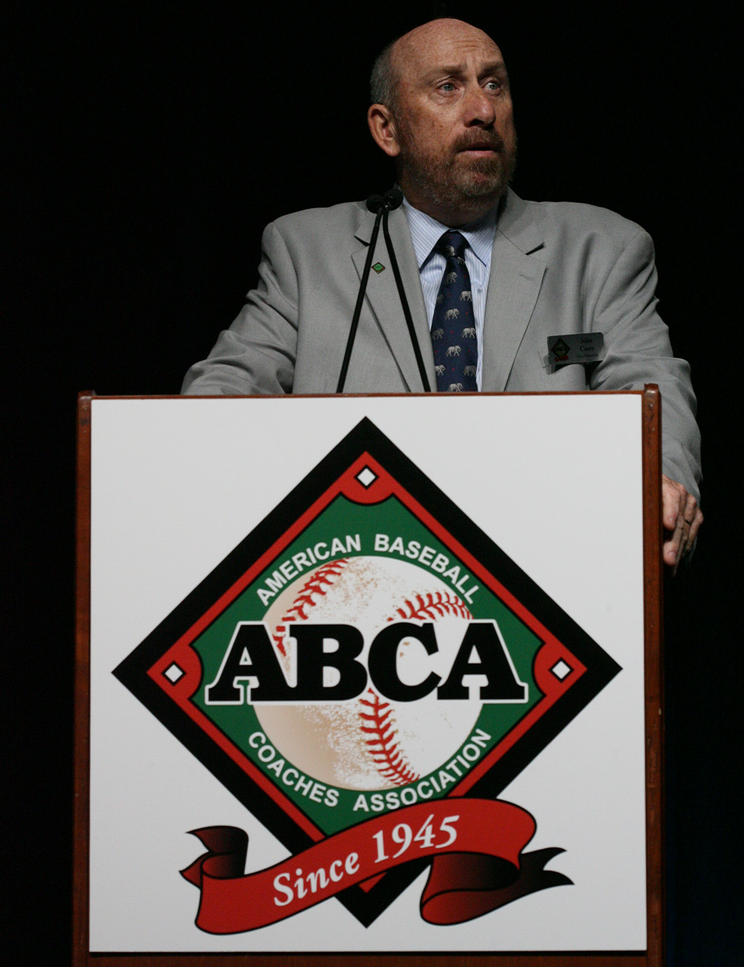 John Casey in a grey suit speaking at a wooden podium with ABCA logo on it at the 2015 ABCA Convention